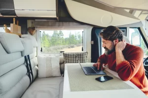 A man sitting at the table in his RV is using his laptop to check RV finance options online as he considers an upgrade